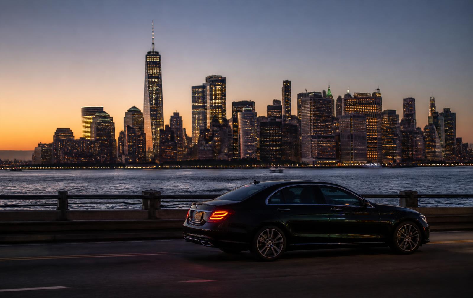 Black executive sedan on a New Jersey waterfront road with the Manhattan skyline across the Hudson River